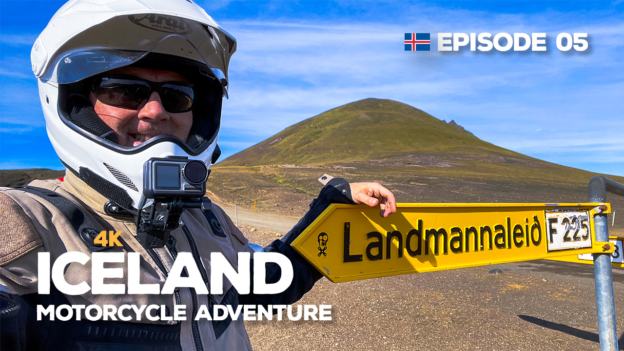 A photo of Benjamin Craig wearing a motorcycle helmet, standing by the sign for the F225 landmannaleið road 